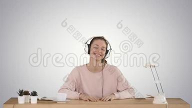 漂亮的女士穿着粉红色套头衫，听着耳机里的音乐，微笑着在渐变背景下拍摄。